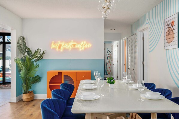 A dining area with a neon sign, a potted plant, and a table set for six.