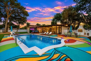 A swimming pool with a colorful deck, lounge chairs, and a building with glass doors.