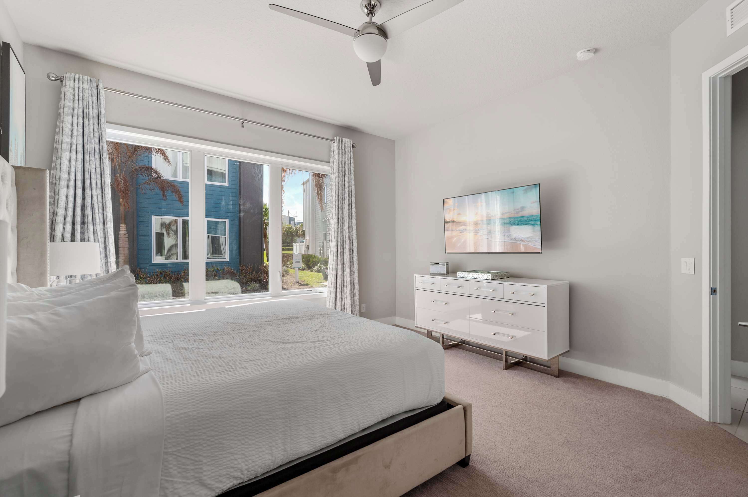 A bedroom with a bed, a TV, a dresser, and a view of the outside.