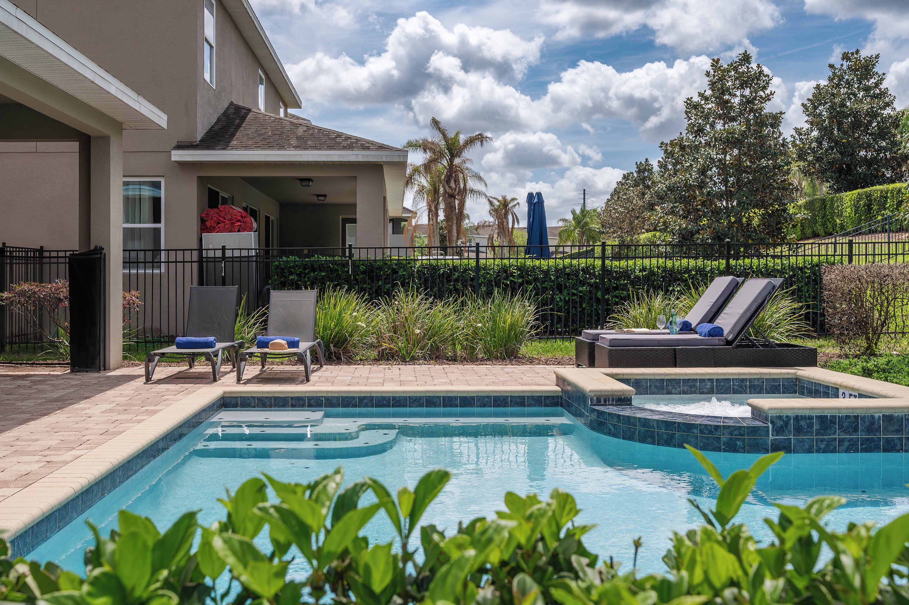 A swimming pool with lounge chairs, a hot tub, and a view of a residential building.
