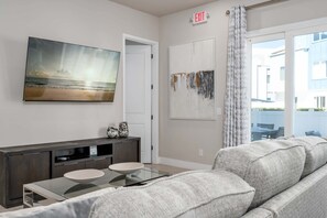 A living room with a sofa, a coffee table, a TV mounted on the wall, and a painting of a beach scene. - Golf-View Reunion Condo Near Disney | Pool & Gym (Kissimmee)