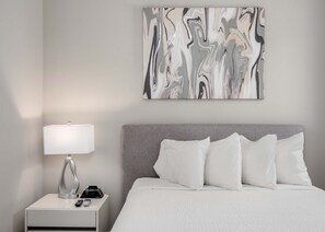 A hotel room with a bed, a nightstand with a lamp, a remote control, and a wall-mounted abstract painting. - Golf-View Reunion Condo Near Disney | Pool & Gym (Kissimmee)