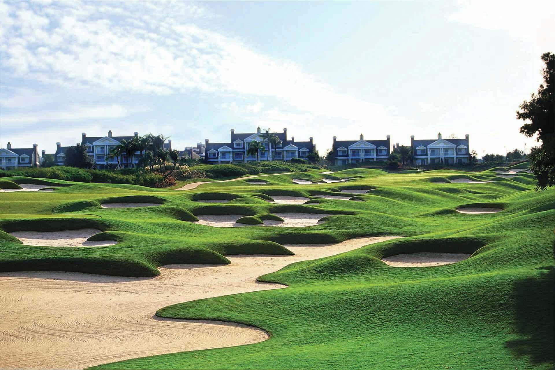 A golf course with bunkers and a row of houses in the background.