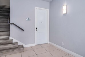 A hallway with a white door, a stairwell, and a wall-mounted light fixture. - Golf-View Reunion Condo Near Disney | Pool & Gym (Kissimmee)