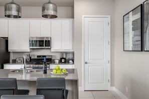 A modern kitchen with stainless steel appliances, a central island with seating, and a door leading to another room. - Golf-View Reunion Condo Near Disney | Pool & Gym (Kissimmee)