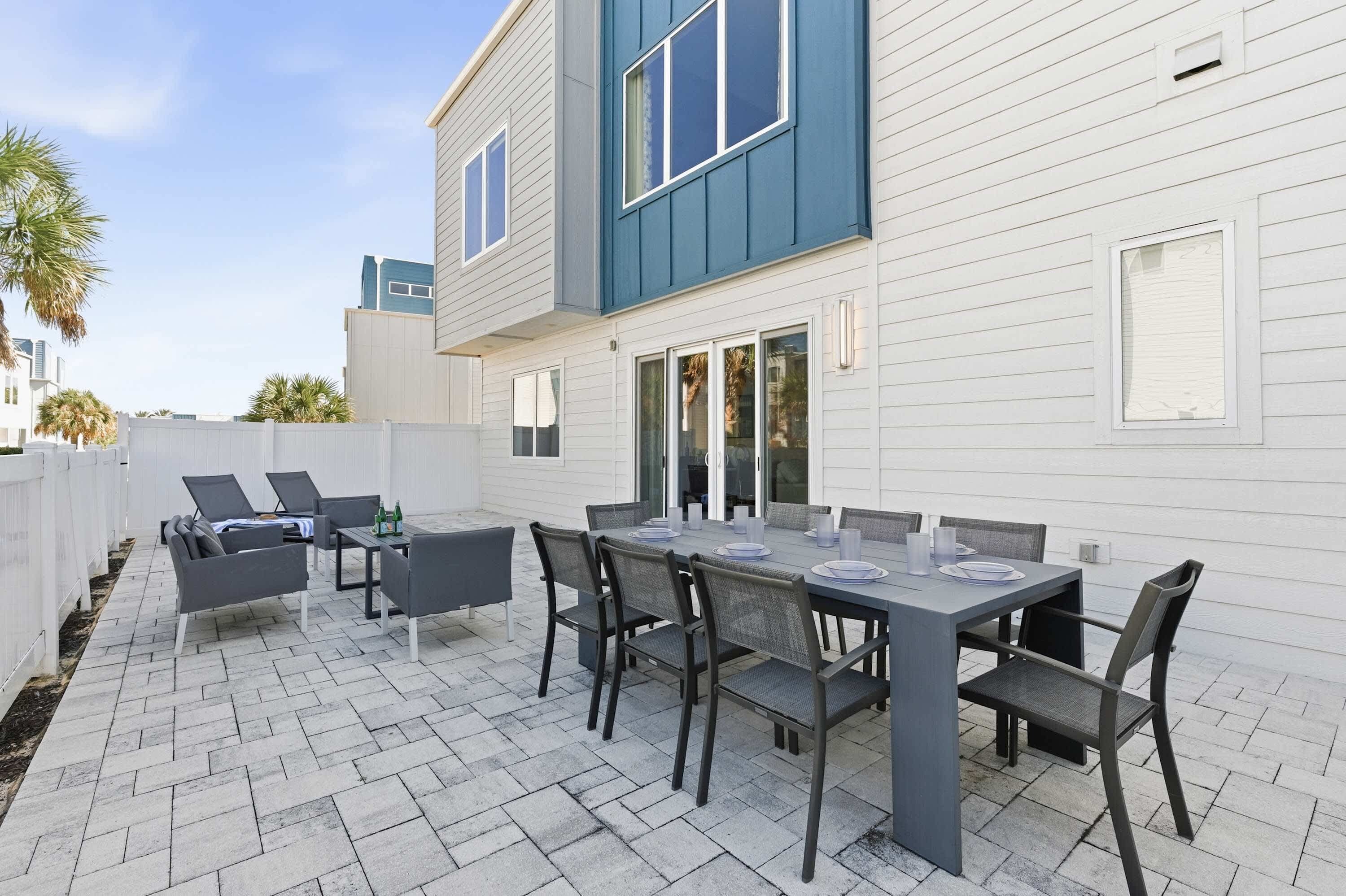 Une terrasse avec une table et des chaises, un espace salon couvert, et un bâtiment blanc orné de motifs bleus.