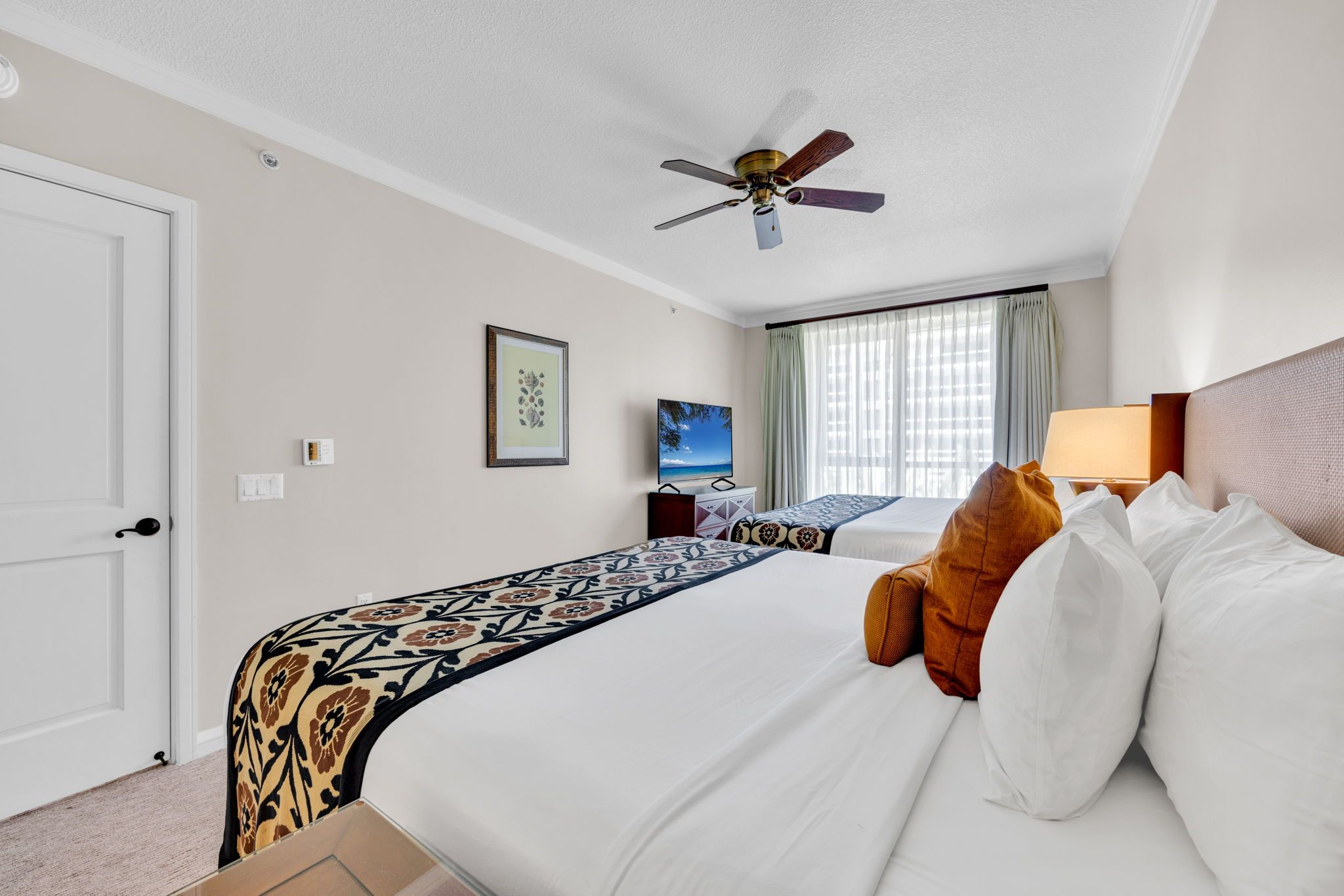 Ein Hotelzimmer mit Bett, Deckenventilator, Fernseher und einem fenster mit Vorhängen.