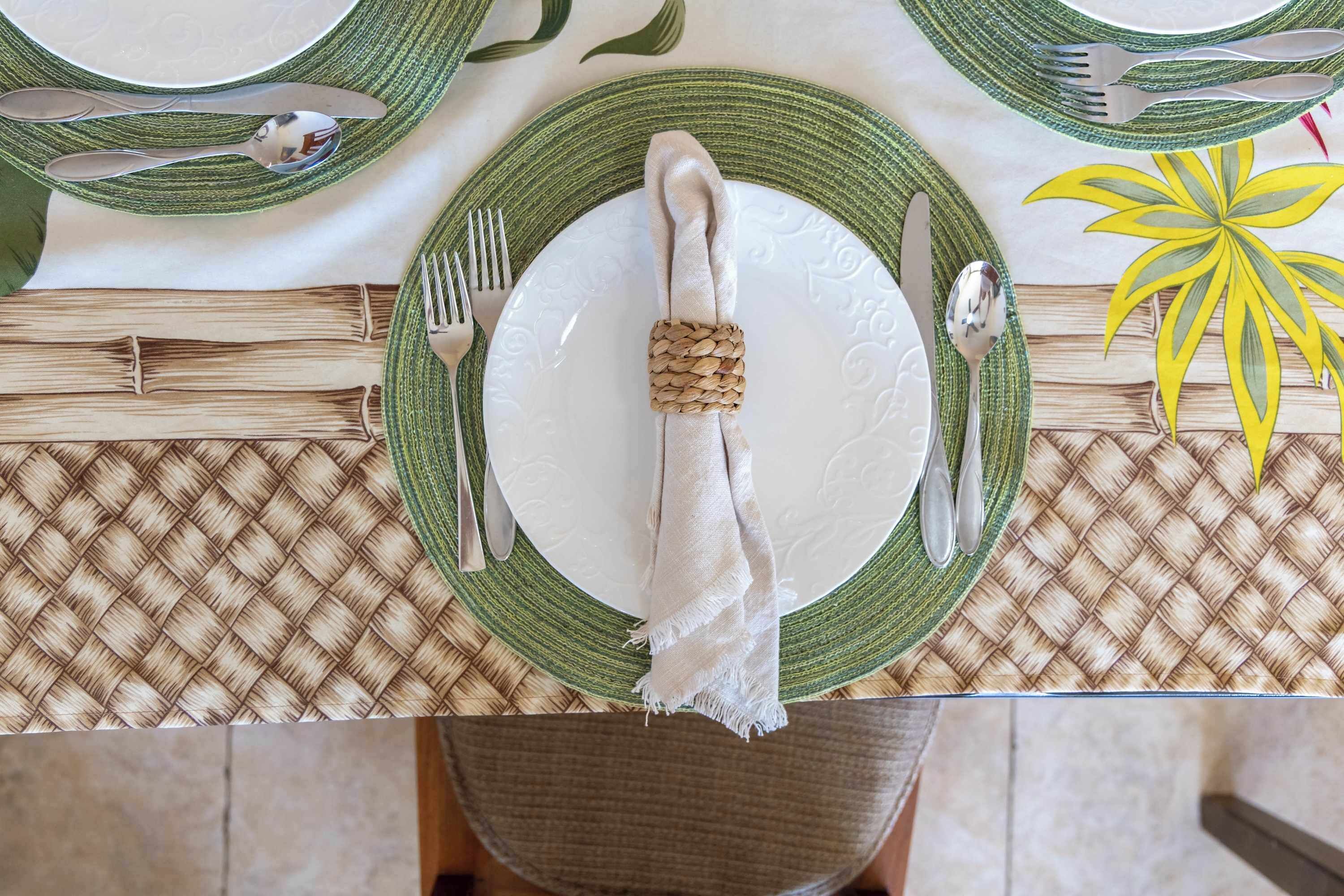 A table set with green and white plates, silverware, and a woven placemat.