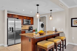 A kitchen with stainless steel appliances, a central island with bar stools, pendant lighting, and a washing machine in the background. - 2 Honua Kai Villas | Ocean Front | Sleeps 14 | Free Car w/ 6+ Nights | ML-3200 (Lahaina)