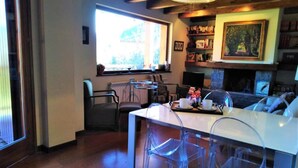 Un ambiente accogliente con zona pranzo, sedie trasparenti, camino e libreria.