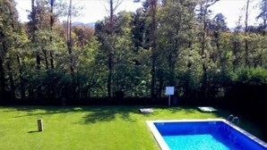 Una piscina rettangolare con bordo bianco, circondata da un prato curato e una fitta foresta sullo sfondo.