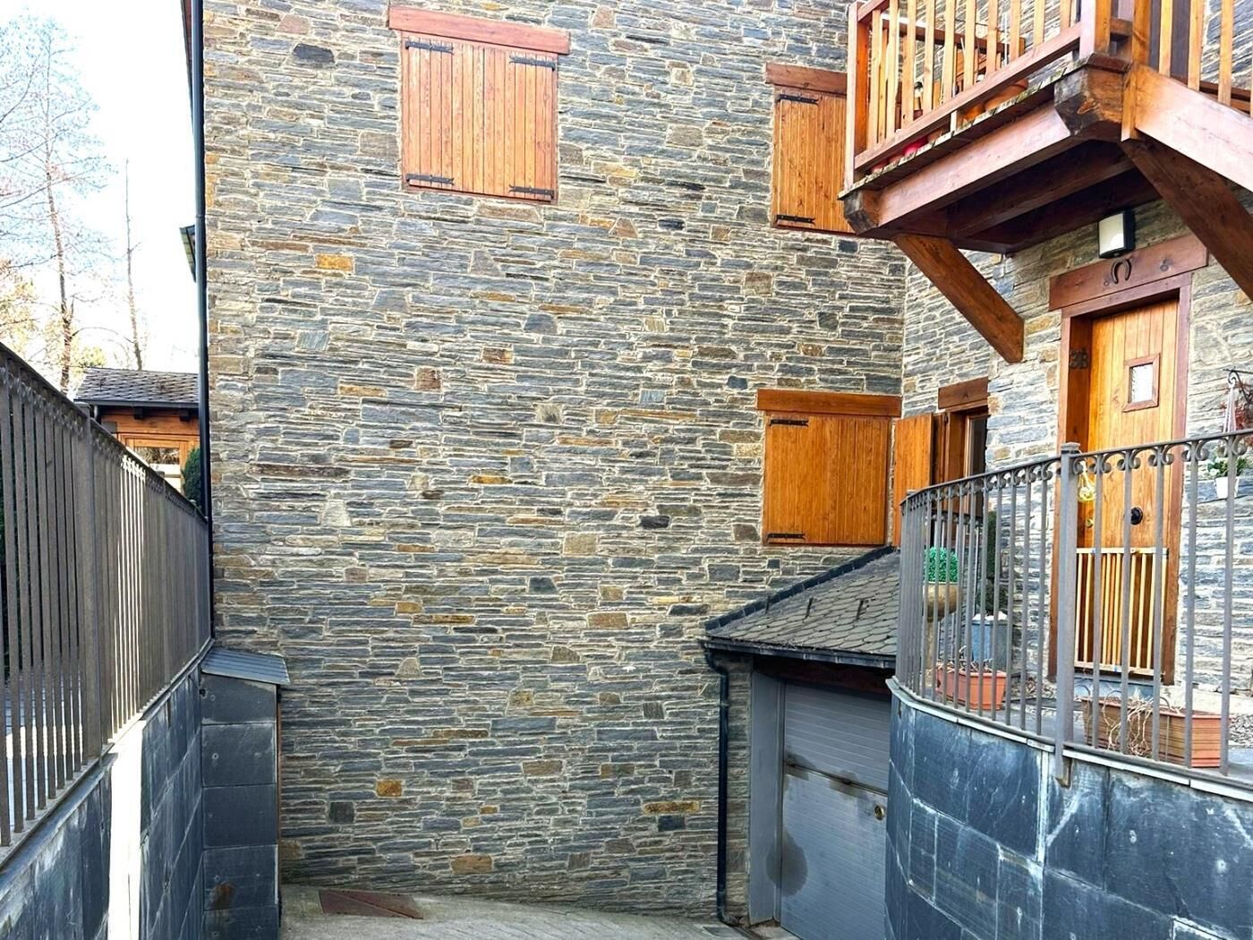 Un edificio de piedra con contraventanas de madera, un balcón y una valla de metal.