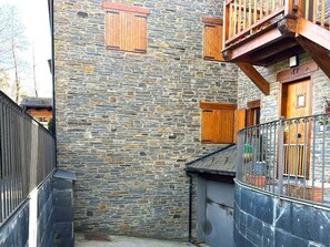 Edifici de pedra amb persianes de fusta, un balcó i una tanca metàl·lica.
