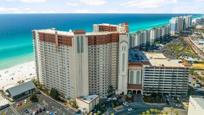 Um hotel alto com vista para a praia, vários andares e área de estacionamento.