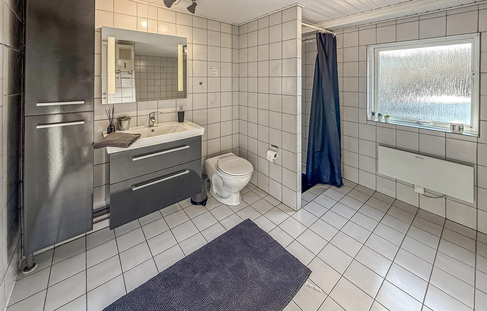 Une salle de bain équipée de toilettes, d’un lavabo, d’un miroir et d’une fenêtre donnant sur un paysage agréable.