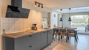 Et moderne køkken med indbygget komfur, kaffemaskine og spiseplads med bord og stole.