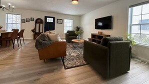 Una sala de estar con sofá, sillón, mesa de centro, televisor y comedor con sillas y una mesa.