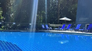 Una piscina con azulejos azules, sillas de descanso y una fuente de agua.