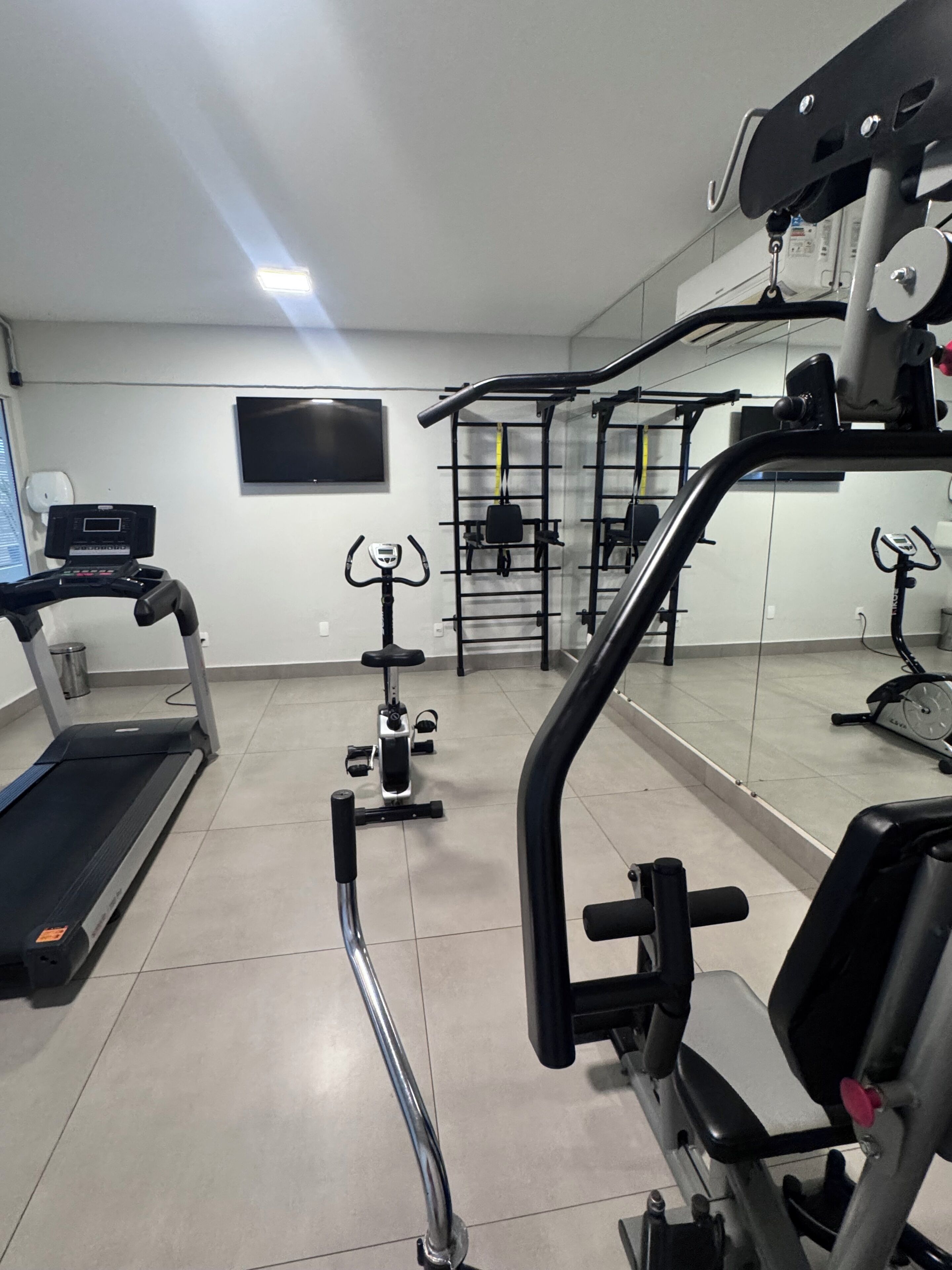 Ein Fitnessstudio mit Trainingsgeräten, Laufband und Spiegel, der den Raum reflektiert.