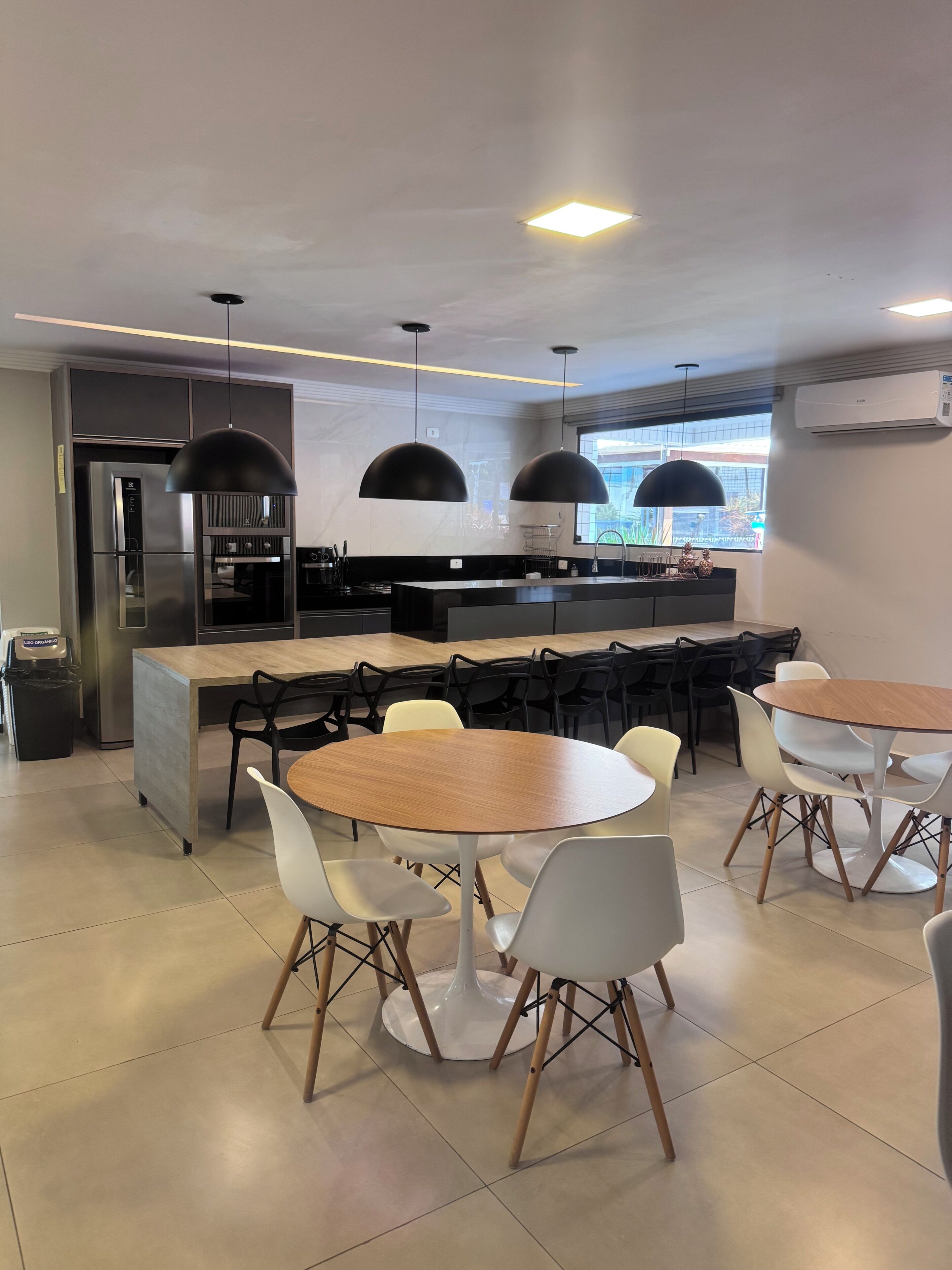 Una cocina moderna con refrigerador empotrado, cafetera y comedor con mesas y sillas redondas.