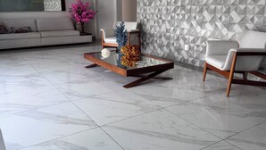 Una sala de estar moderna con un sofá, dos sillones, una mesa de centro, un papel tapiz con diseño y una araña.