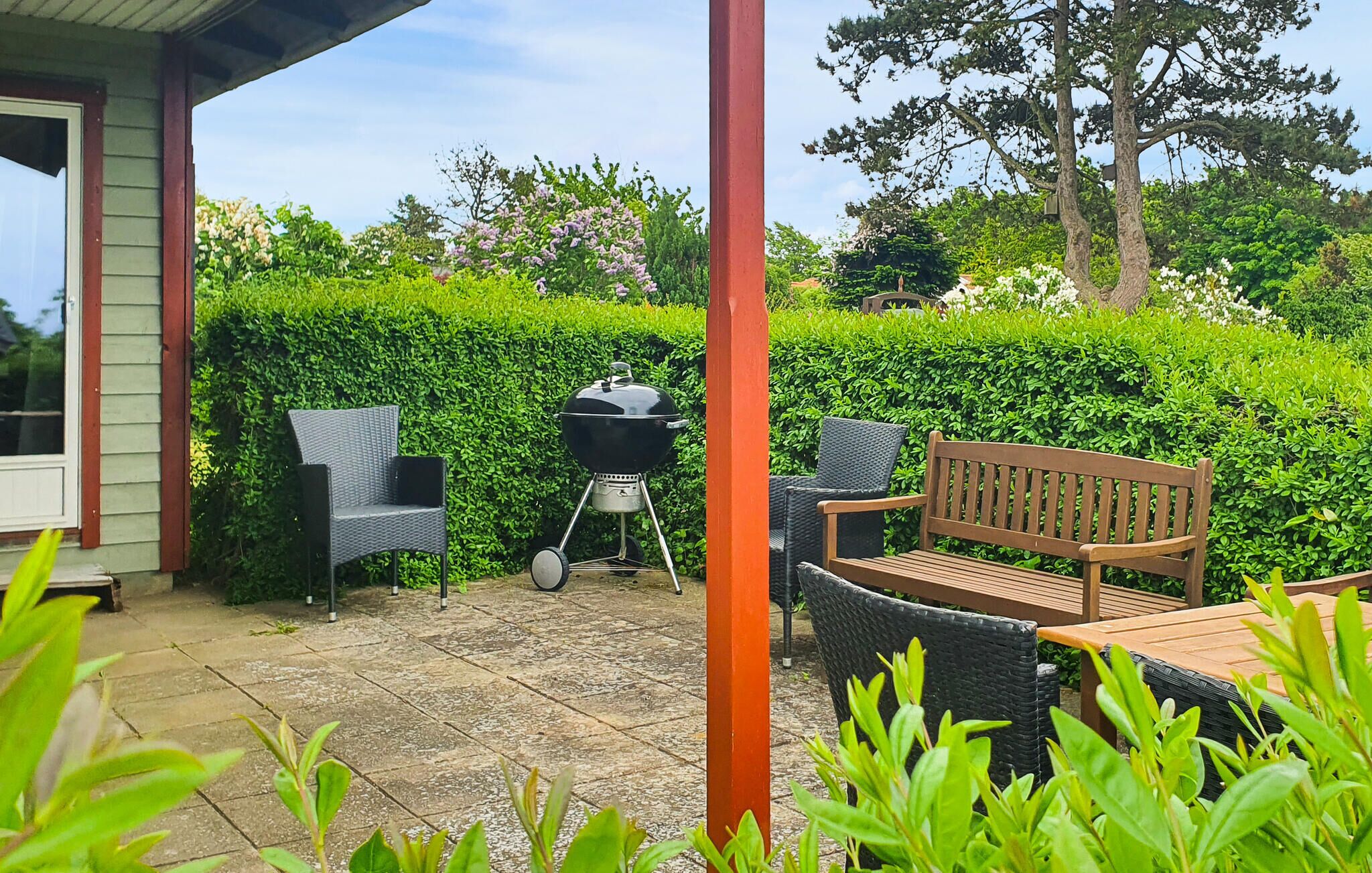Une terrasse avec des meubles d’extérieur, un barbecue et une haie en arrière-plan.