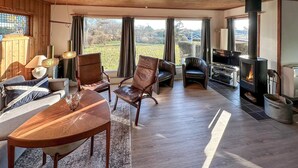 A spacious living room with a wooden floor, leather chairs, a wooden coffee table, a fireplace, and a large window offering a view of the outdoors. - Nice home in Karrebæksminde with WiFi (Karrebæksminde)