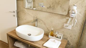 A bathroom with a white sink, wooden vanity, a towel rack, a mirror, a hairdryer, and a soap dispenser.