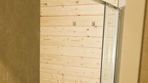 Un petit espace douche fermé, avec un revêtement mural en bois et une porte en verre.