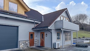 Een huis met twee verdiepingen, een garage, een stenen fundering en een houten terras.