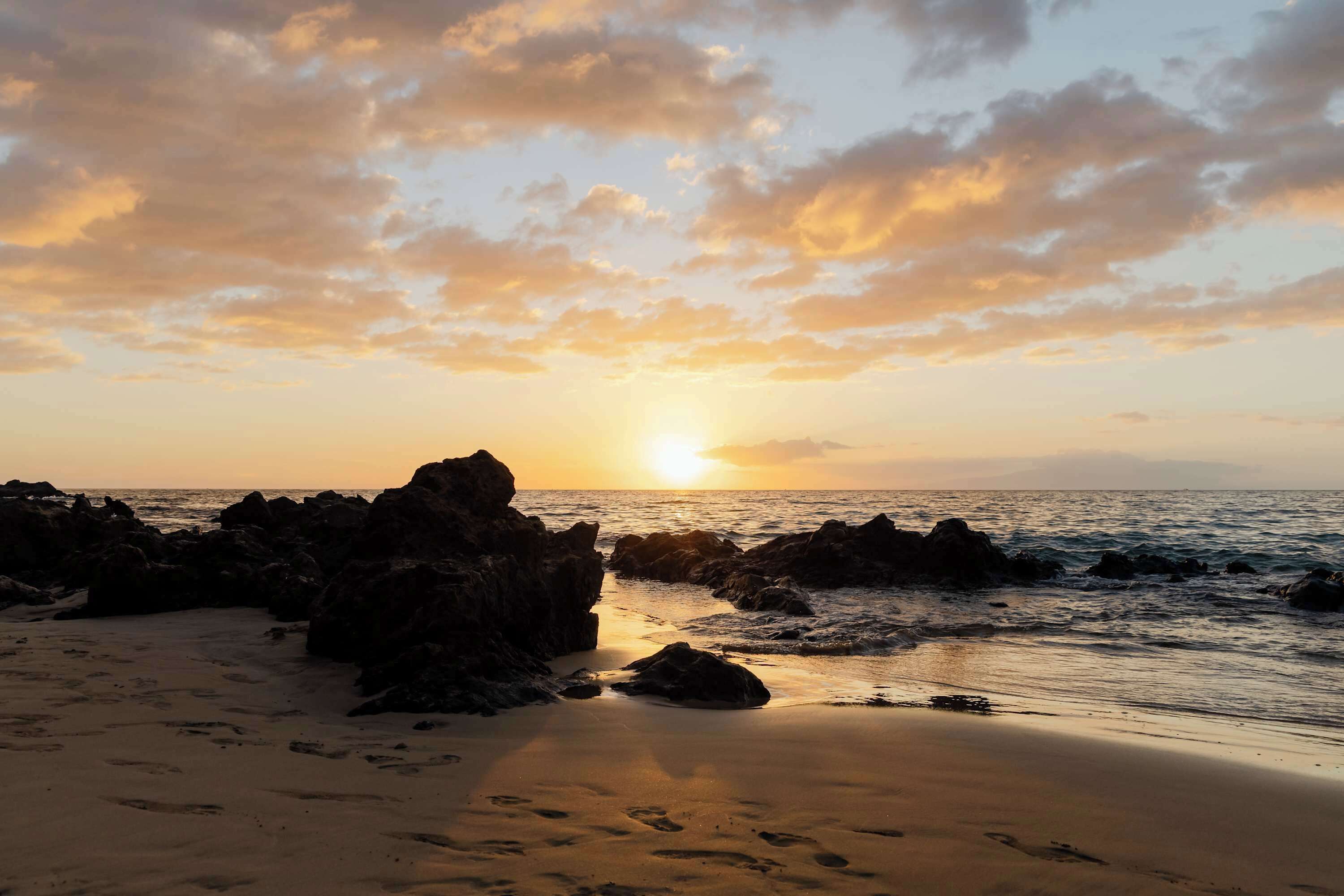 A beach with rocks and the ocean at sunset.