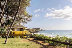 A beach view with a yellow lifeguard stand, a wooden fence, and a building in the background. - Studio w/ pool & beach access (Kihei)
