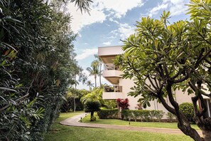 A modern building with a flat roof, surrounded by lush greenery and a well-maintained lawn. - Studio w/ pool & beach access (Kihei)