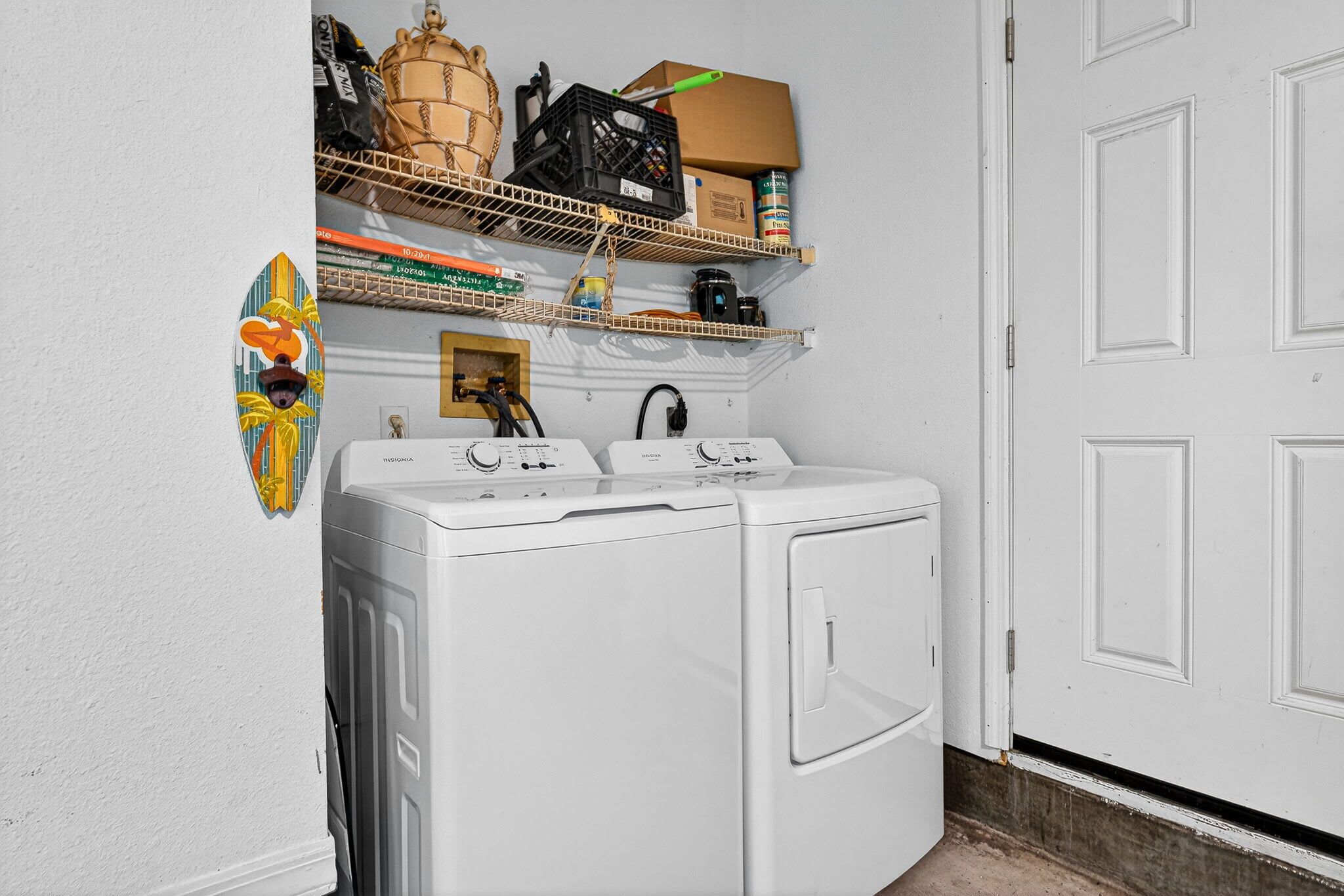 A laundry room with a washing machine, shelves with various items, and a door.