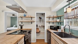 Cocina pequeña con estufa, microondas, lavaplatos y estantes de madera.