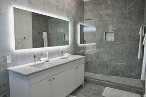 A modern bathroom with a large mirror, two sinks, and a shower area.