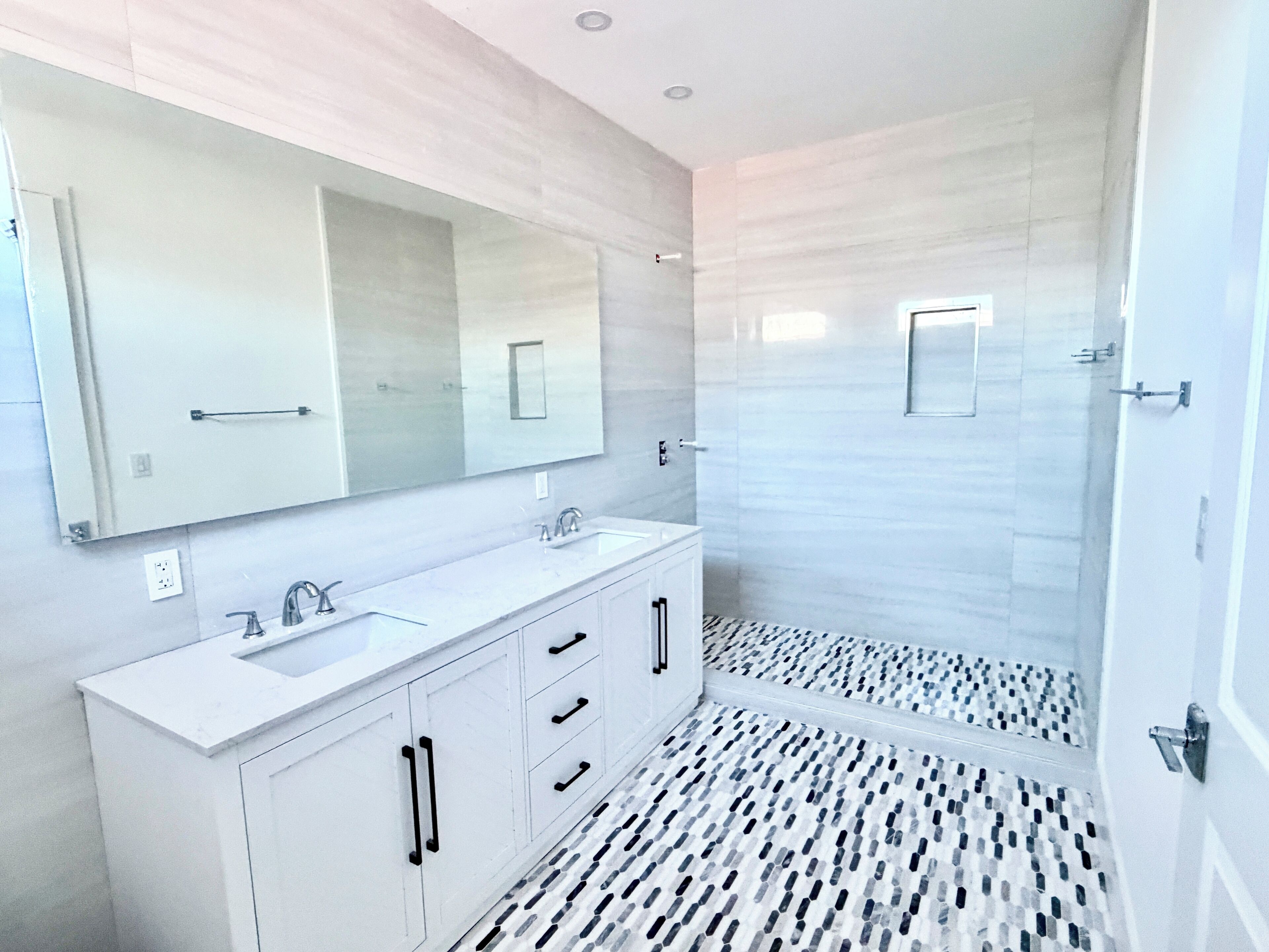 A modern bathroom with a large mirror, two sinks, and a shower area.