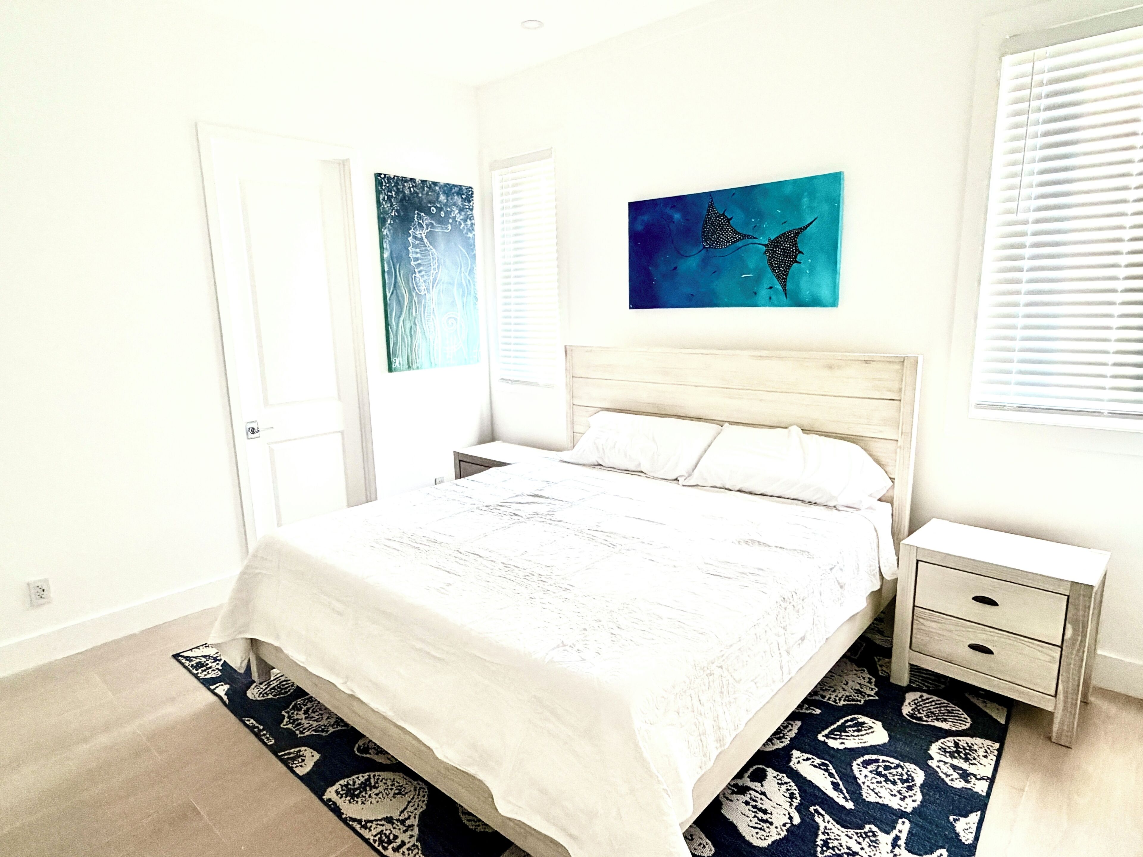 A bedroom with a bed, bedside tables, a nightstand, a door, and two wall-mounted artworks.