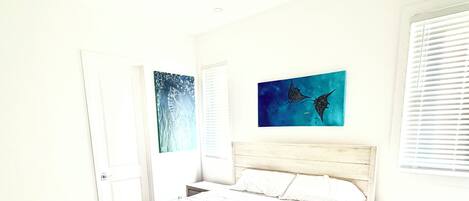 A bedroom with a bed, bedside tables, a nightstand, a door, and two wall-mounted artworks.