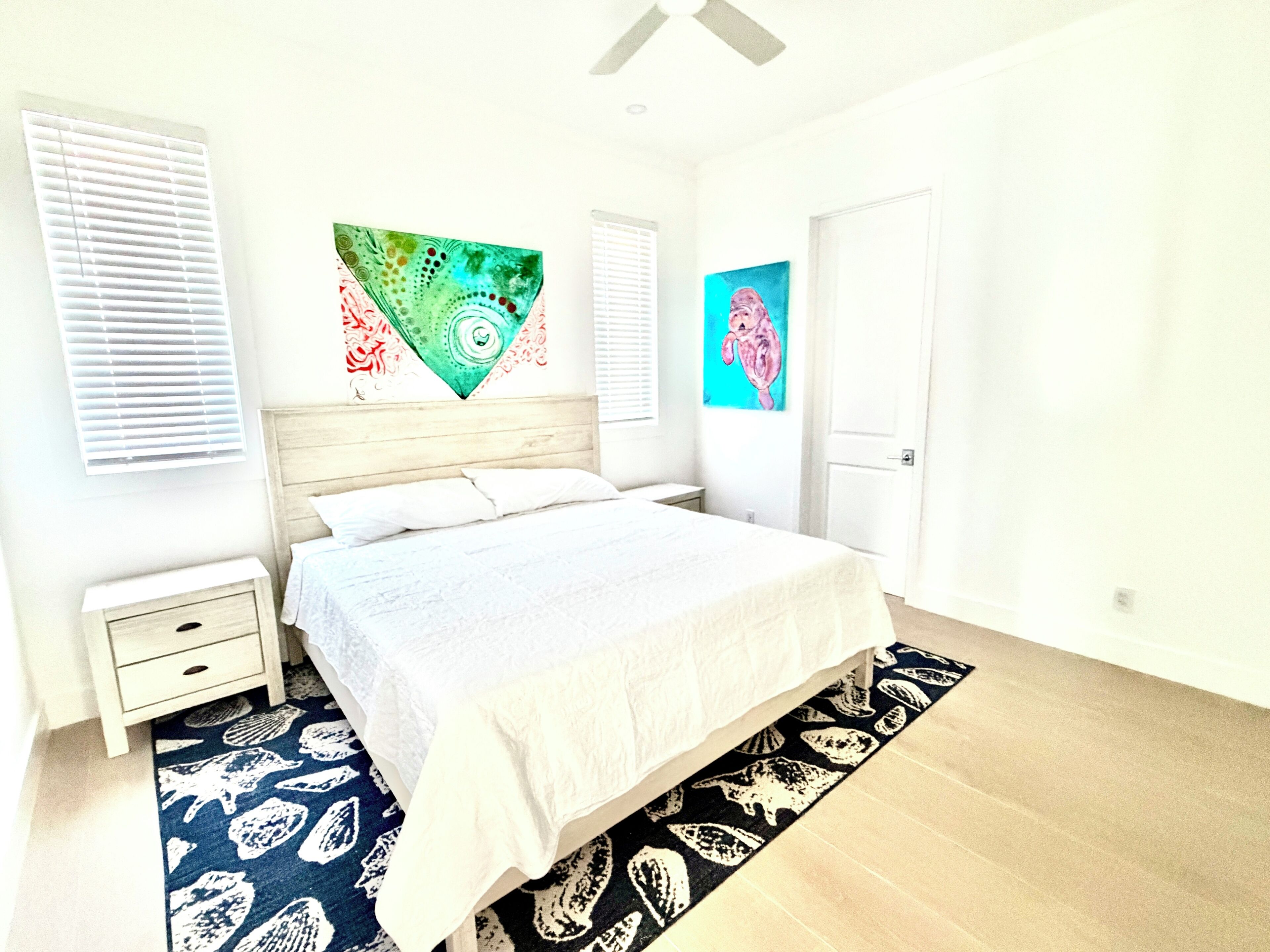 Un dormitorio con cama, mesita de noche, una obra de arte en la pared y una puerta.