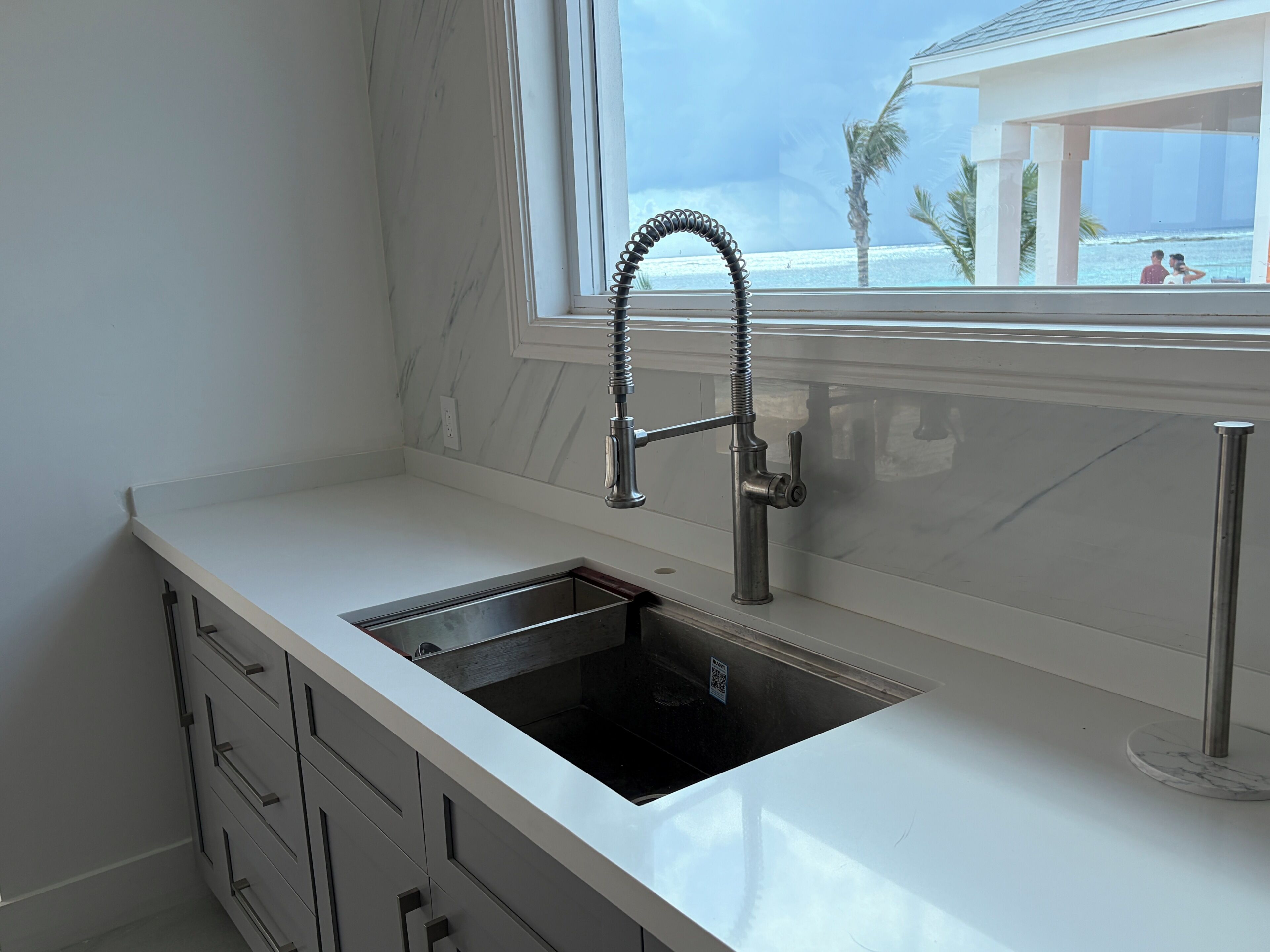 A modern kitchen with a built-in sink, a window with a view of the beach, and a marble backsplash.