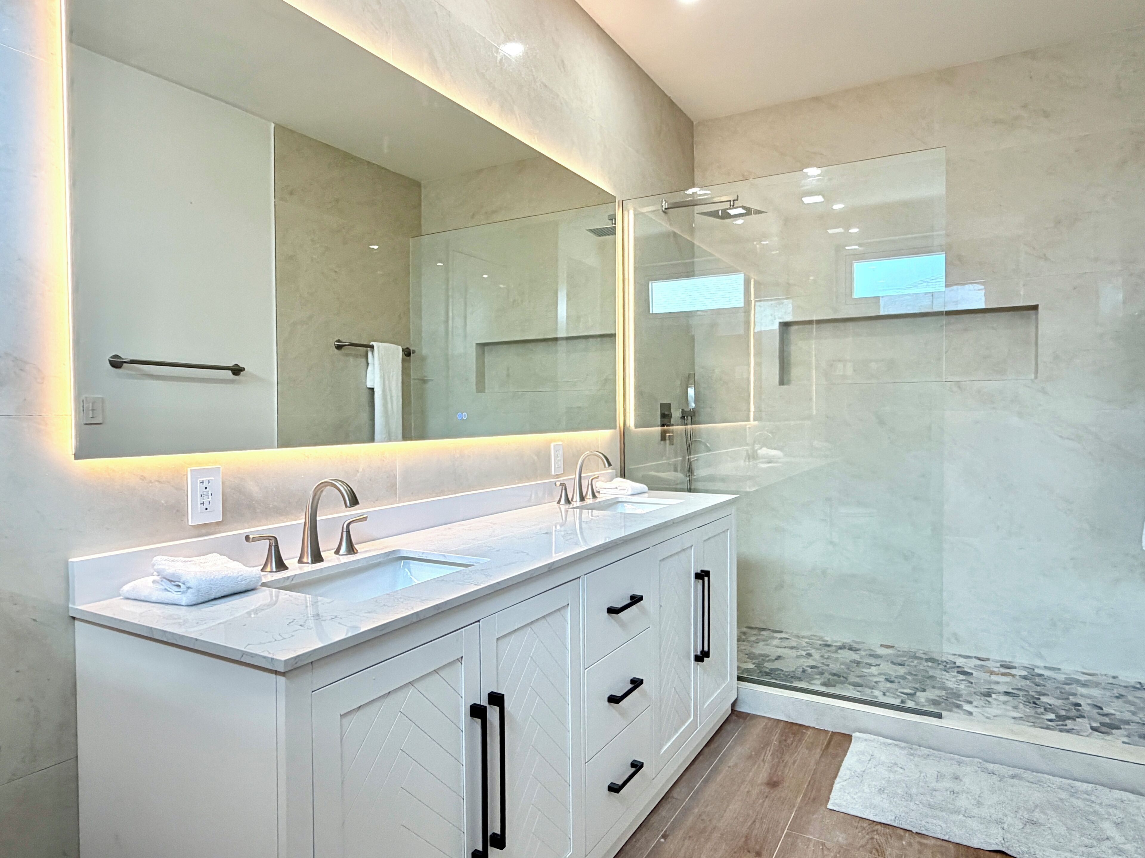 A modern bathroom with a large mirror, two sinks, a shower, and a walk-in shower.