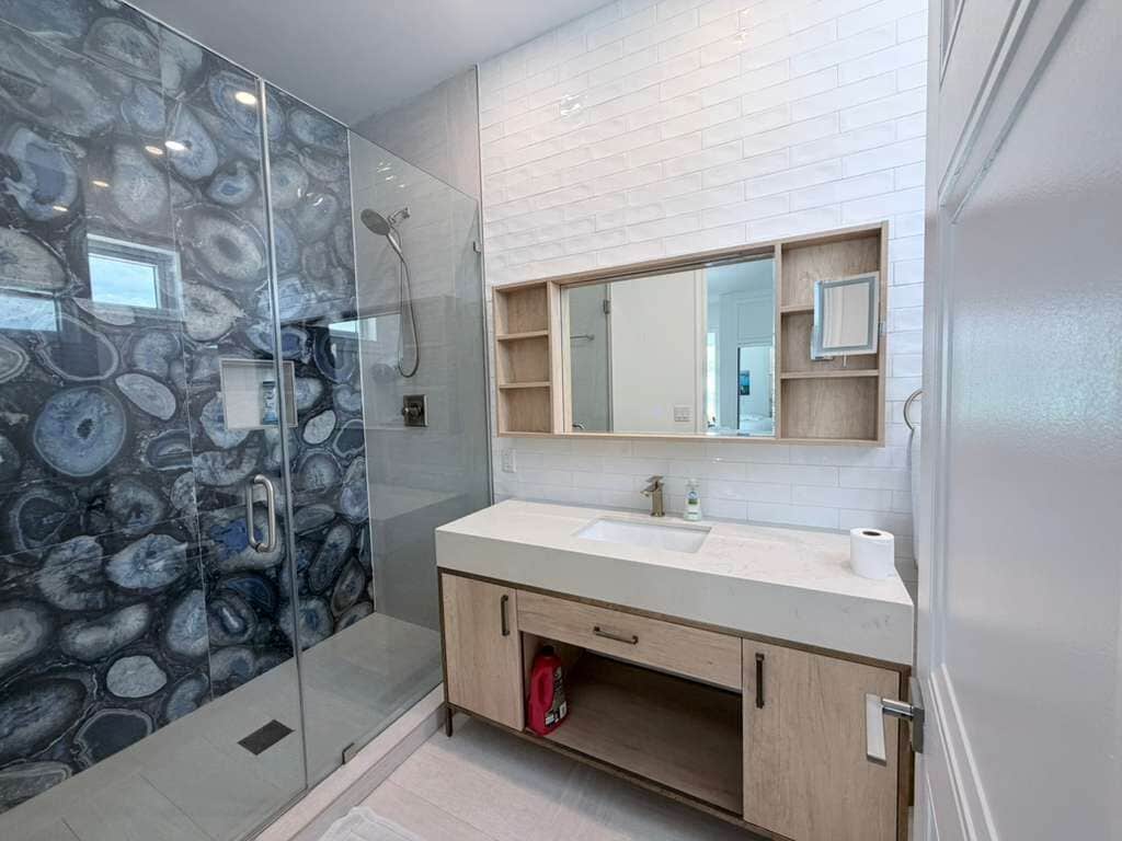 A bathroom with a glass shower enclosure, a sink with a mirror above, and wooden cabinets below.
