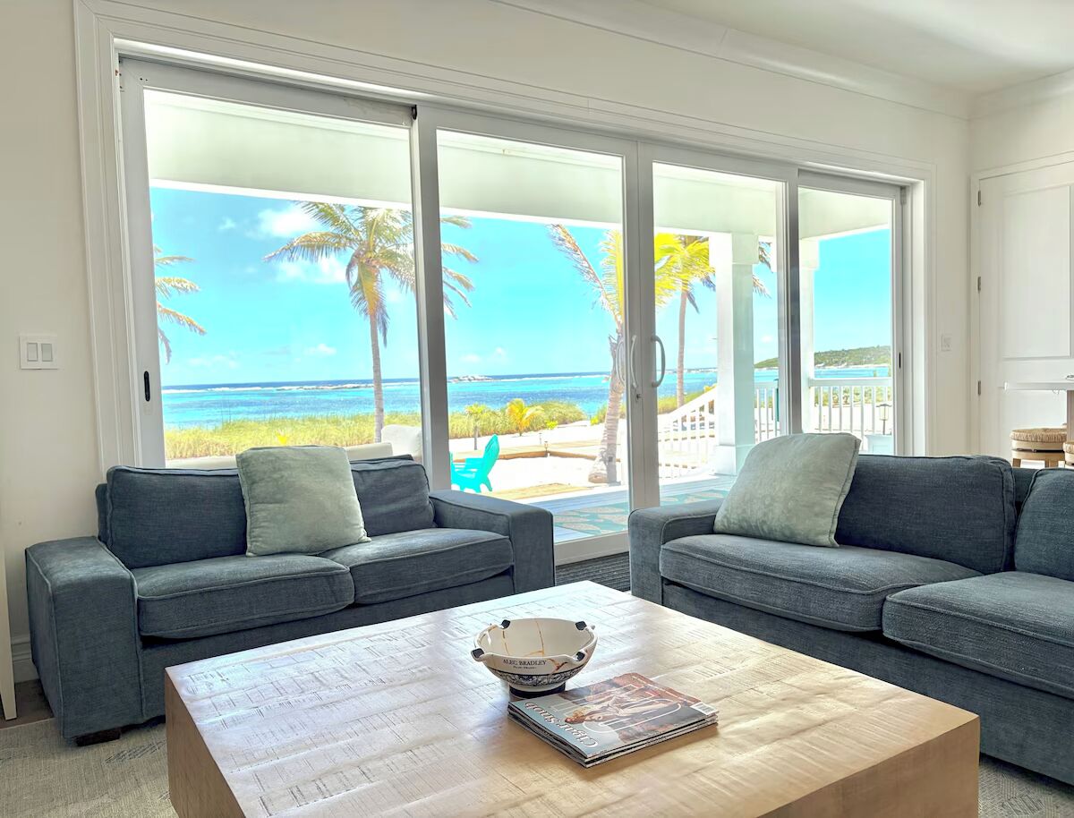 A living room with two grey sofas, a wooden coffee table, and a view of the ocean through large sliding glass doors.