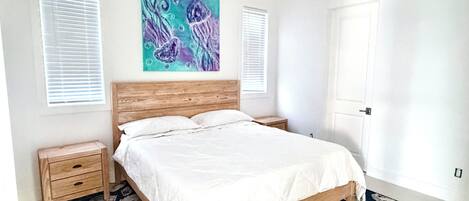 A bedroom with a wooden bed, white bedding, a blue and purple painting, two bedside tables, and a patterned rug.
