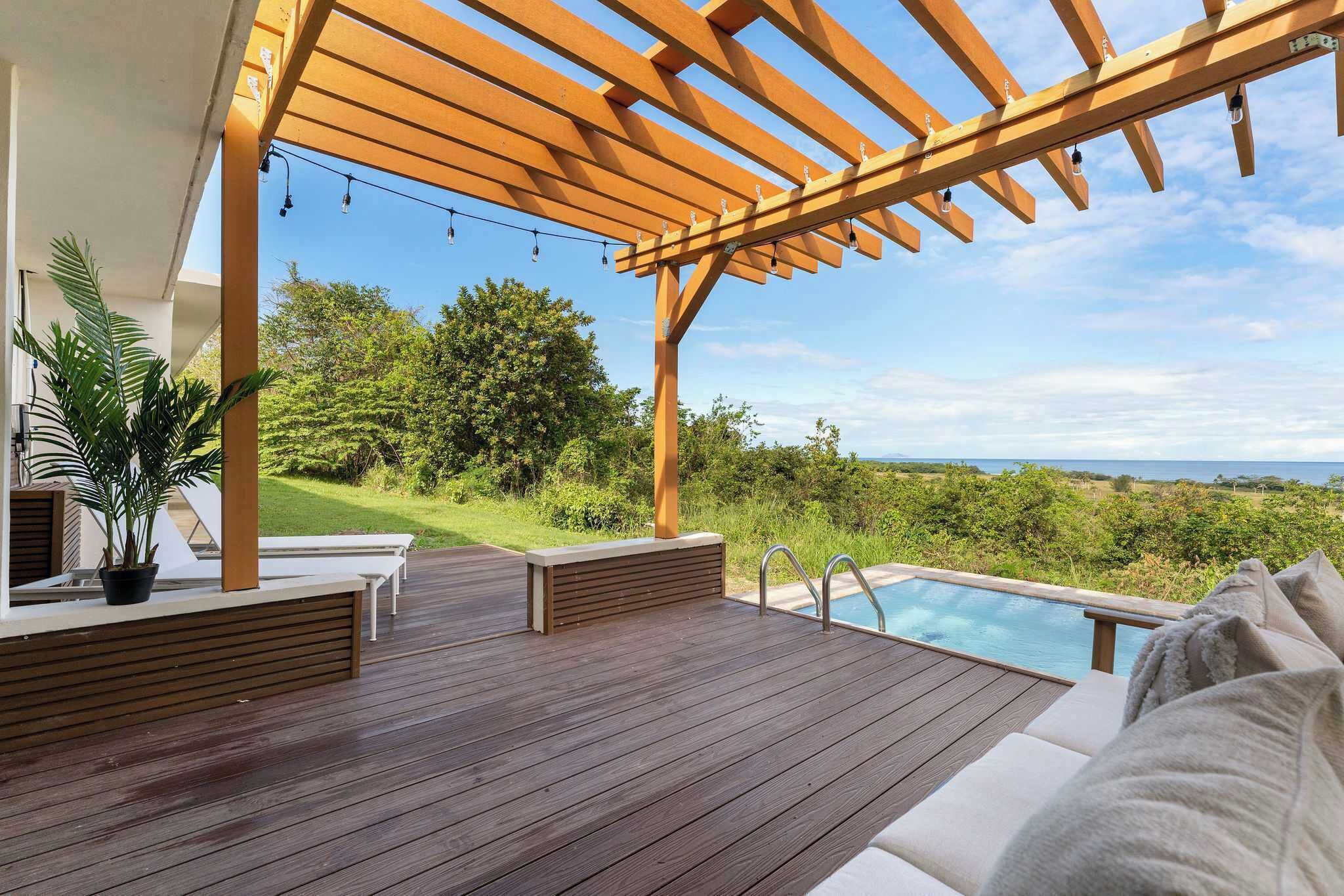 Une terrasse en bois avec une pergola, un espace salon extérieur, une piscine et une vue sur le paysage.