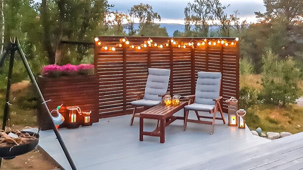 Eine Terrasse im Freien mit zwei gepolsterten Stühlen, einem kleinen Tisch, Lichterketten und Laternen.
