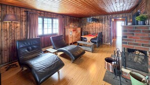 Ein gemütlicher Raum mit Holzwänden, einem Kamin, einem Esstisch mit Stühlen und Ledersitzmöbeln.
