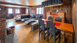 Ein gemütliches Blockhaussinnenzimmer mit Holztisch, Stühlen, einer Couch und einem Kamin.