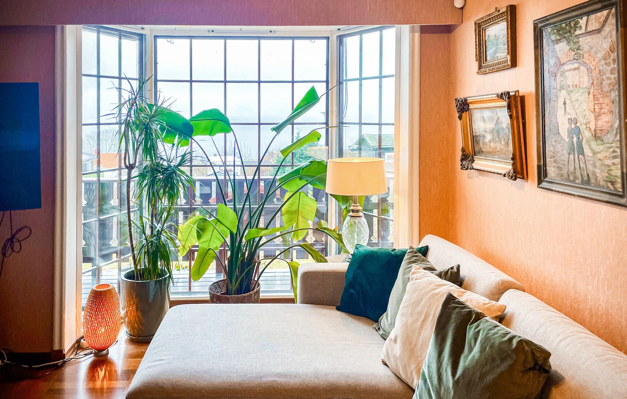 A room with a large window, a sofa, a lamp, and a potted plant.